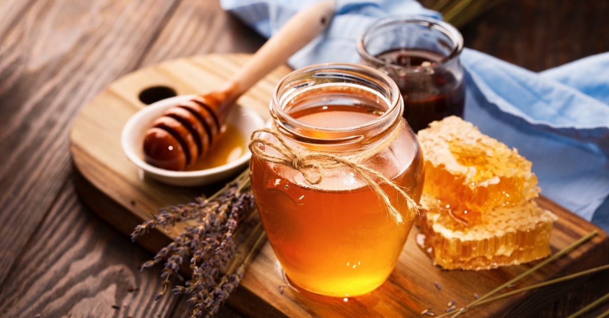 A jar of honey and some honeycomb on a bread board.

